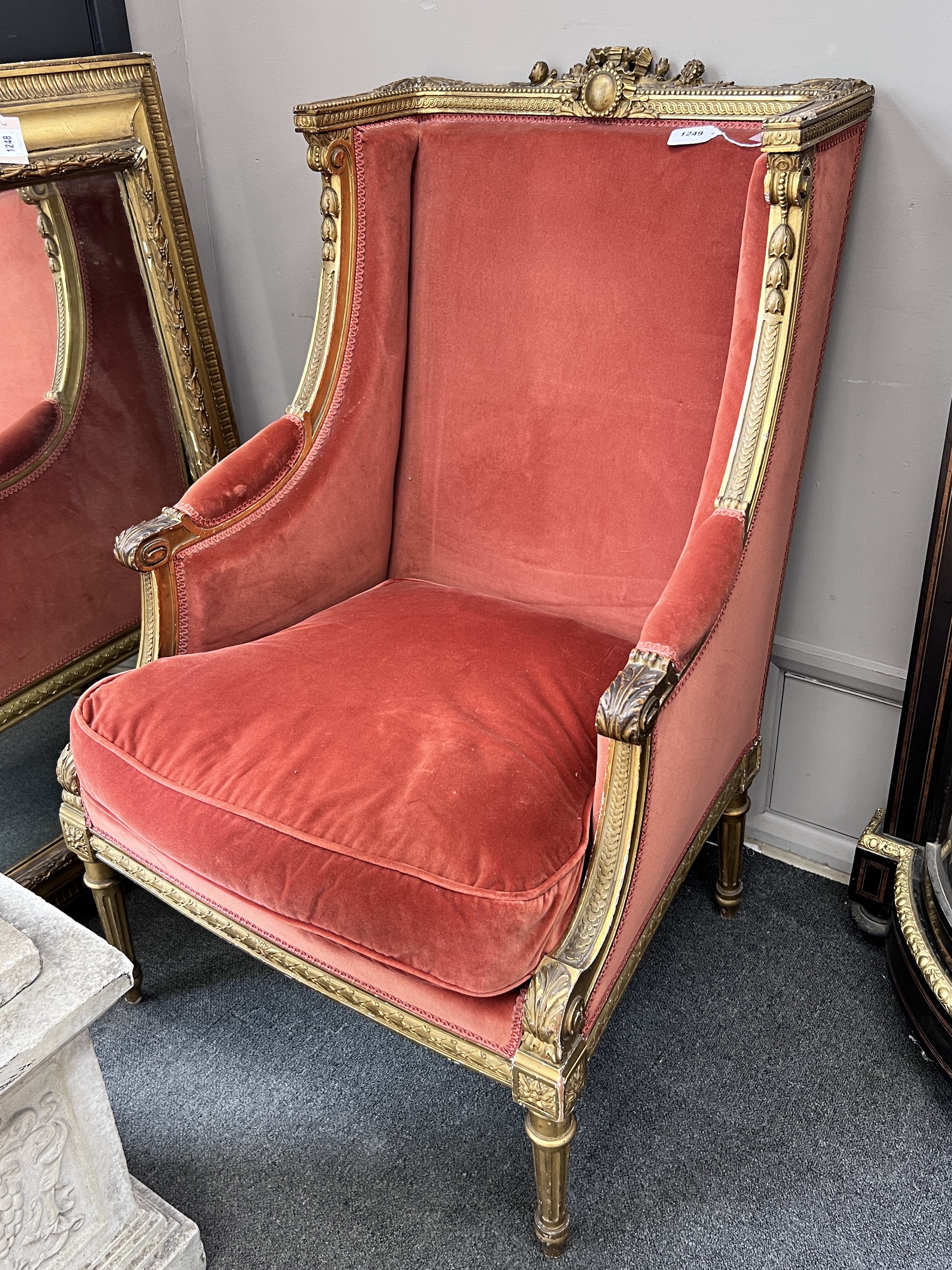 A late 19th century French Louis XVI style giltwood carved upholstered winged armchair, width 70cm, height 108cm